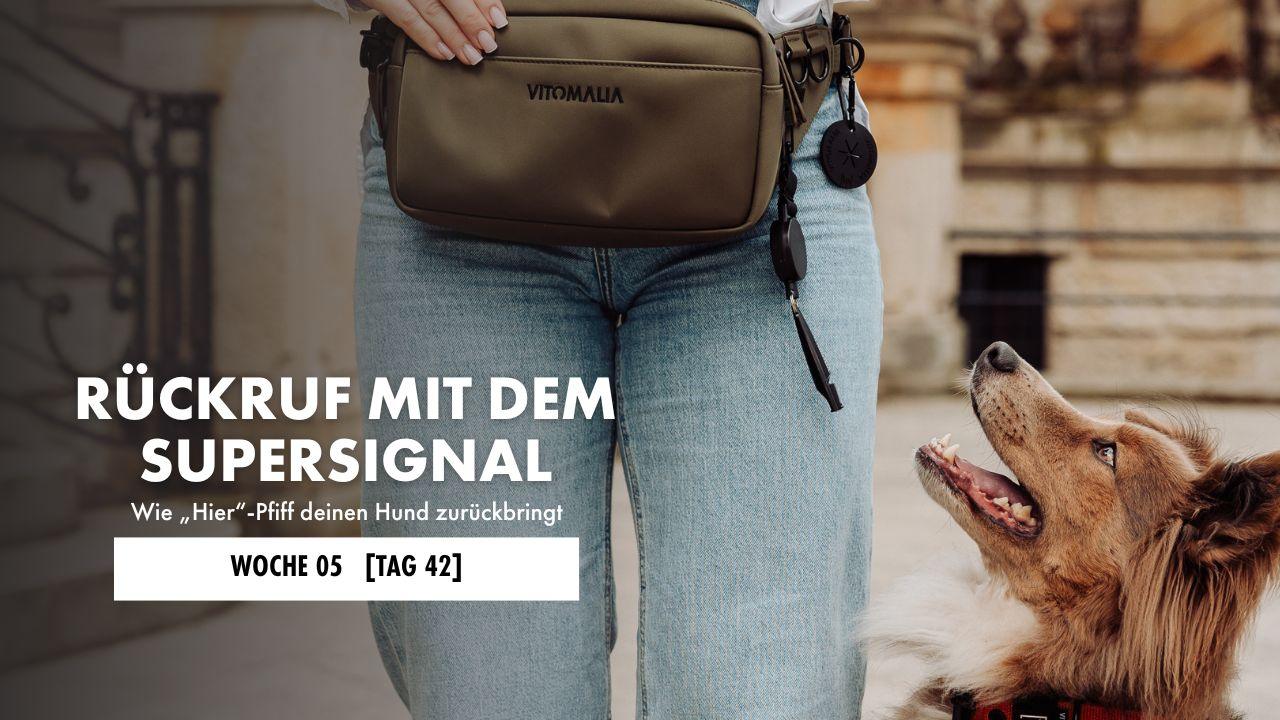 Hund sitzt neben Hundeführerin, die eine Gassitasche mit Hundepfeife trägt